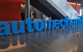 Large blue Automechanika sign displayed at the entrance of Automechanika Frankfurt 2024, with attendees walking nearby in a modern exhibition hall